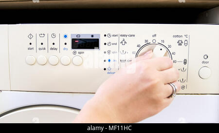 Closeup image of young woman turning round knob on washing maching control panel and choosing water temperature Stock Photo