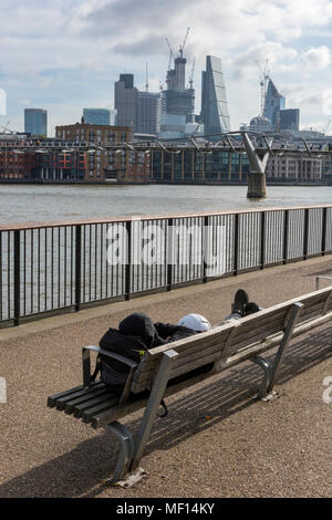 A construction worker taking a break on a park bench at the side of the river thames in central london with the capital city skyline in the background Stock Photo