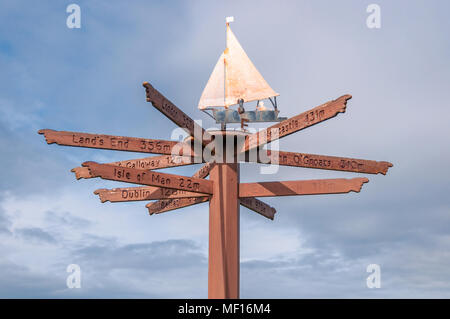 Tourist direction & distance signs mounted on post with weather vane on top, located on shorefront in Port William, Dumfries & Galloway, Scotland, UK Stock Photo