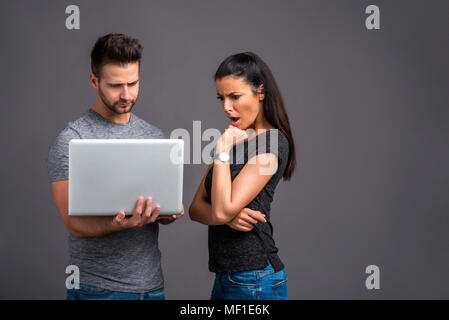 A handsome young man holding a laptop next to his girlfriend who is feeling upset Stock Photo