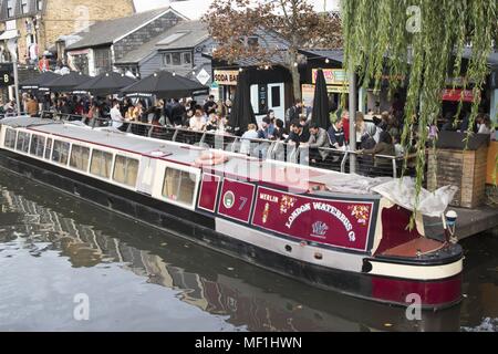 View of the 'Merlin, ' the London Waterbus Company's red and cream, number seven, narrowboat, barge, or canal boat, docked next to crowds of people, in the Camden Lock area of Camden Market, located in Camden Town in Northwest London, United Kingdom, October 28, 2017. () Stock Photo