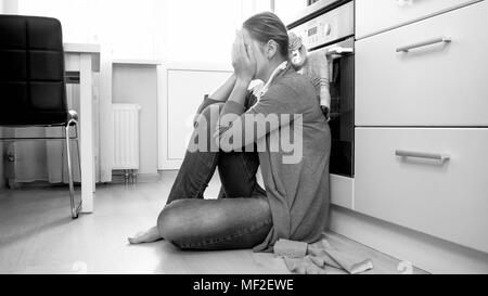 Black and white photo of young housewife crying on floor at living room Stock Photo