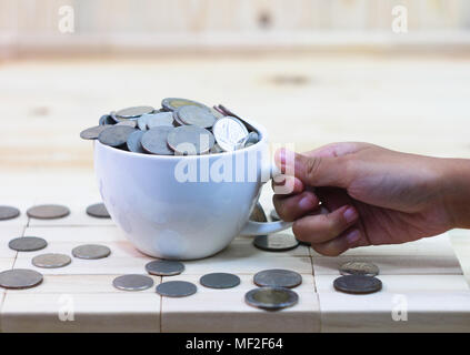 The coin in a white coffee cup rests on a wooden table and around a cup.  A girl hand catch the glass. Stock Photo