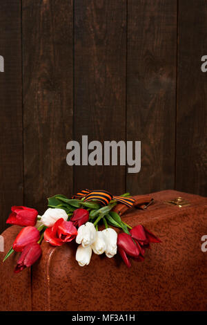 old suitcase with flowers, symbol of victory in world war II with St. George's ribbon, a dark wooden background, retro concept Stock Photo