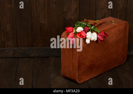 old suitcase with flowers, symbol of victory in world war II with St. George's ribbon, a dark wooden background, retro concept Stock Photo