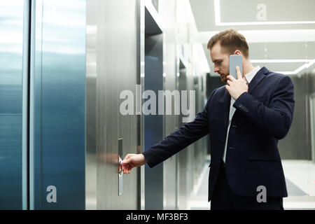 Businessman communicating on cell phone while waiting for the lift Stock Photo