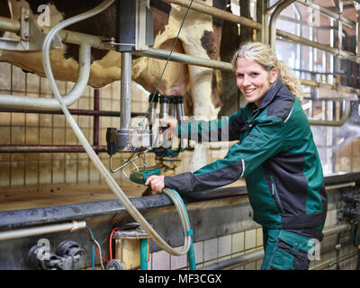 Portrait of smiling female farmer in stable milking a cow Stock Photo