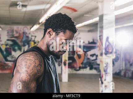 Serious man with tattoos in cellar with graffitis looking down Stock Photo