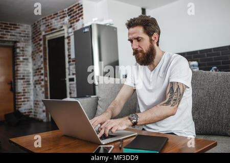Bearded man sitting on the couch at home using laptop Stock Photo