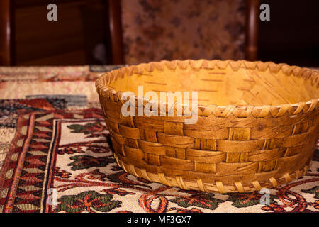 small traditional birch bark flat basket for products ("lukoshko") stands on a woven colored homemade table cloth Stock Photo