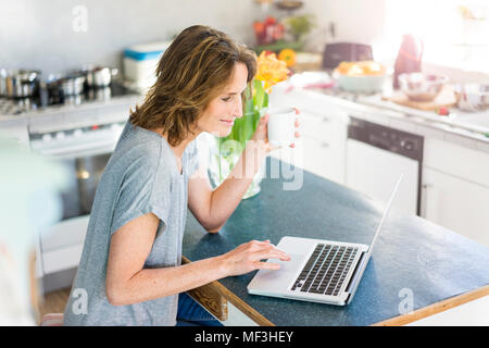 Smiling woman using laptop in kitchen at home Stock Photo
