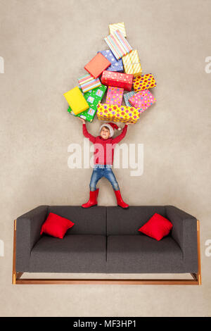 Boy with Santa hat holding pile of Christmas presents Stock Photo