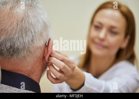 Female doctor applying hearing aid to senior man's ear Stock Photo