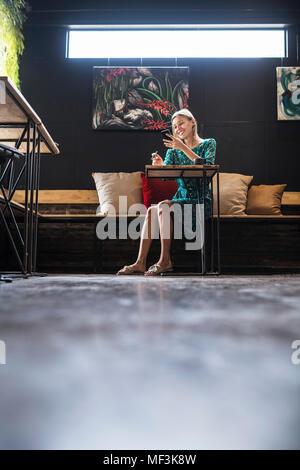 Young smiling woman with green dress sitting in cafe,  checking her smartphone Stock Photo