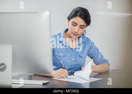 Businesswoman taking notes at desk in office Stock Photo