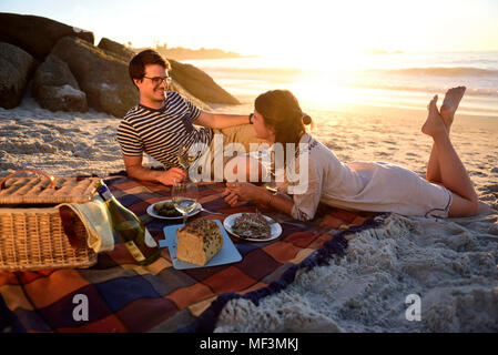 Happy couple having a picnic on the beach at sunset Stock Photo