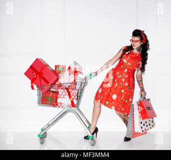 Tattooed woman with shopping bags and shopping cart full of gifts Stock Photo