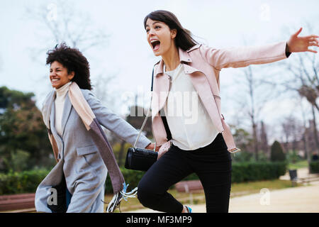 Spain, Barcelona, two exuberant women running in city park Stock Photo