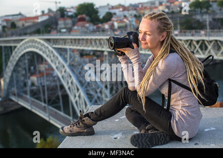 Young woman with camera sitting on the viewing platform opposite the Dom Luis I bridge across the Douro river, Porto, Portugal. Stock Photo