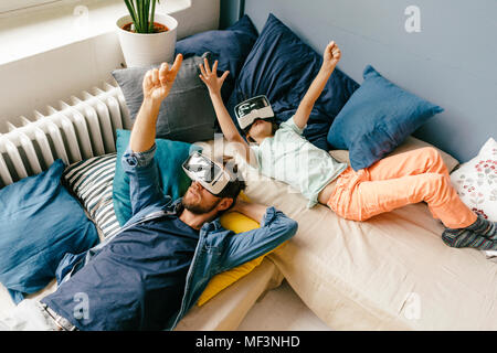 Father and son wearing VR glasses lying down at home Stock Photo