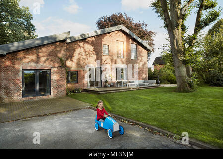 Girl playing with soapbox in driveway of residential house Stock Photo