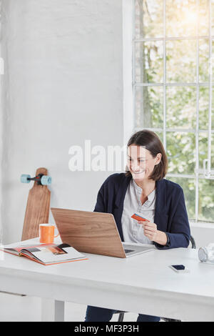 Happy businesswoman using laptop on desk holding card Stock Photo
