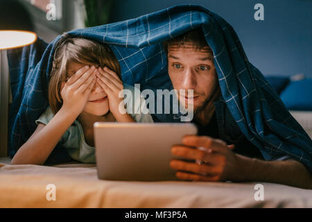 Excited father and son watching a movie on tablet under blanket Stock Photo