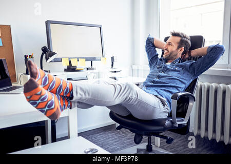 Relaxed man sitting at desk in office looking at computer screen