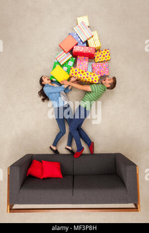 Couple standing on couch, holding big pile of presents Stock Photo