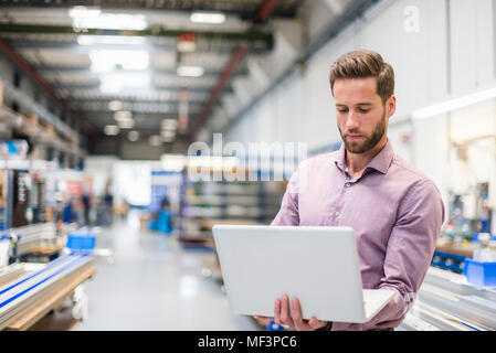 Young businessman using laptop in production hall Stock Photo