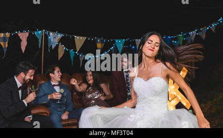 Happy bride dancing on a night field party with groom and friends in the background Stock Photo