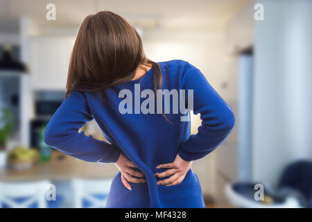 Young woman having suffering lower back ache pressing lumbar spine area as exhausted physical symptom on indoor room background Stock Photo