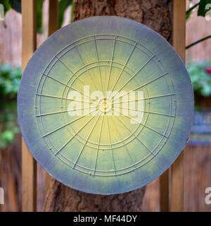 Dartboard game board painted in green, yellow and blue hanged on tree with blurred background of public garden Stock Photo