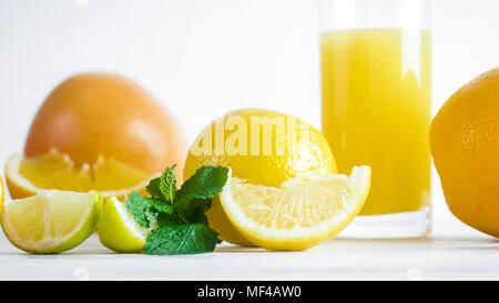 Closeup image of oranges, lemons, and grapefruits next to glass of orange juice on white wooden desk Stock Photo
