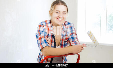 Portrait of young woman looking in camera and holding paint roller Stock Photo