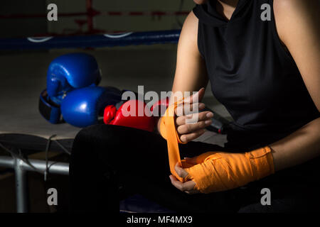 closeup woman boxer hand while wearing orange strap on wrist with boxing gloves and boxing ring background Stock Photo