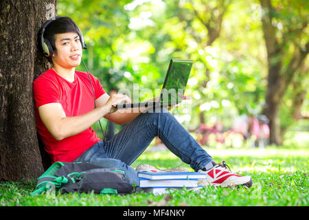 smart and handsome student work with laptop and listen music with headphones in park, Bangkok Thailand Asia Stock Photo