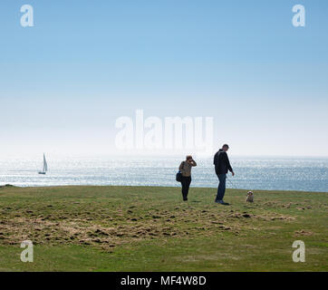 People walking dog at Sound, view toward sea with distant sailing boat Stock Photo