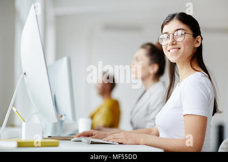 Portrait of smiling young woman sitting at the table and using computer Stock Photo