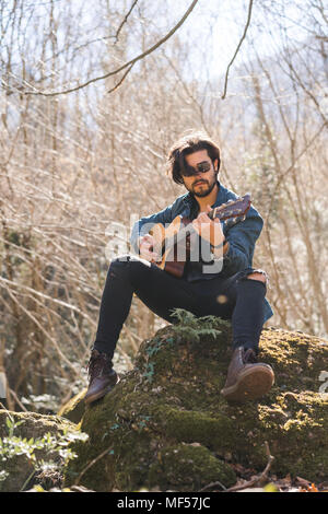Young man sitting on rock playing guitar Stock Photo