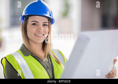 Portrait of smiling woman wearing hard hat and reflective jacket holding plan Stock Photo