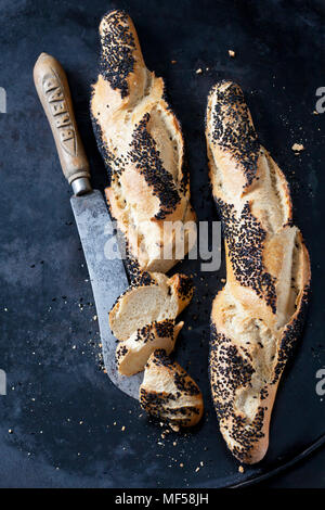 Two baguettes with black cumin and a bread knife on dark metal Stock Photo