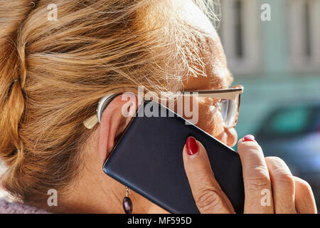Close-up of senior woman with hearing aid using smartphone Stock Photo