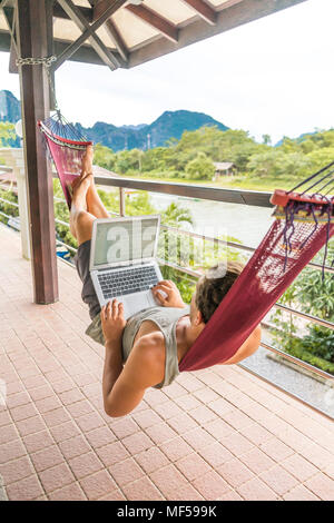 Laos, Vang Vieng, young man lying in hammock using laptop Stock Photo