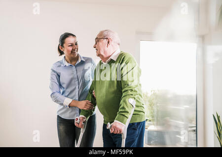 Young woman supporting senior man walking on crutches Stock Photo