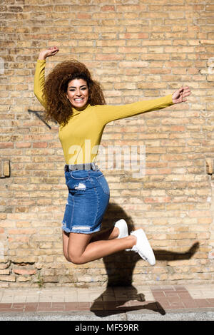 Spain, Andalusia, Granada. Beautiful young woman with curly hairstyle jumping outdoors. Lifestyle concept Stock Photo