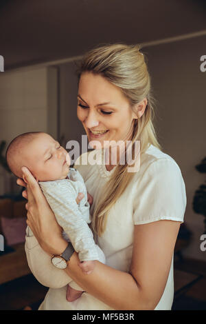Smiling mother holding sleepy newborn baby