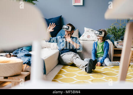 Father and son wearing VR glasses sitting on the floor at home Stock Photo