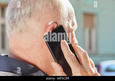Close-up of senior man with hearing aid using smartphone Stock Photo