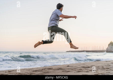 Happy young man jumping in the air on the beach at sunset Stock Photo